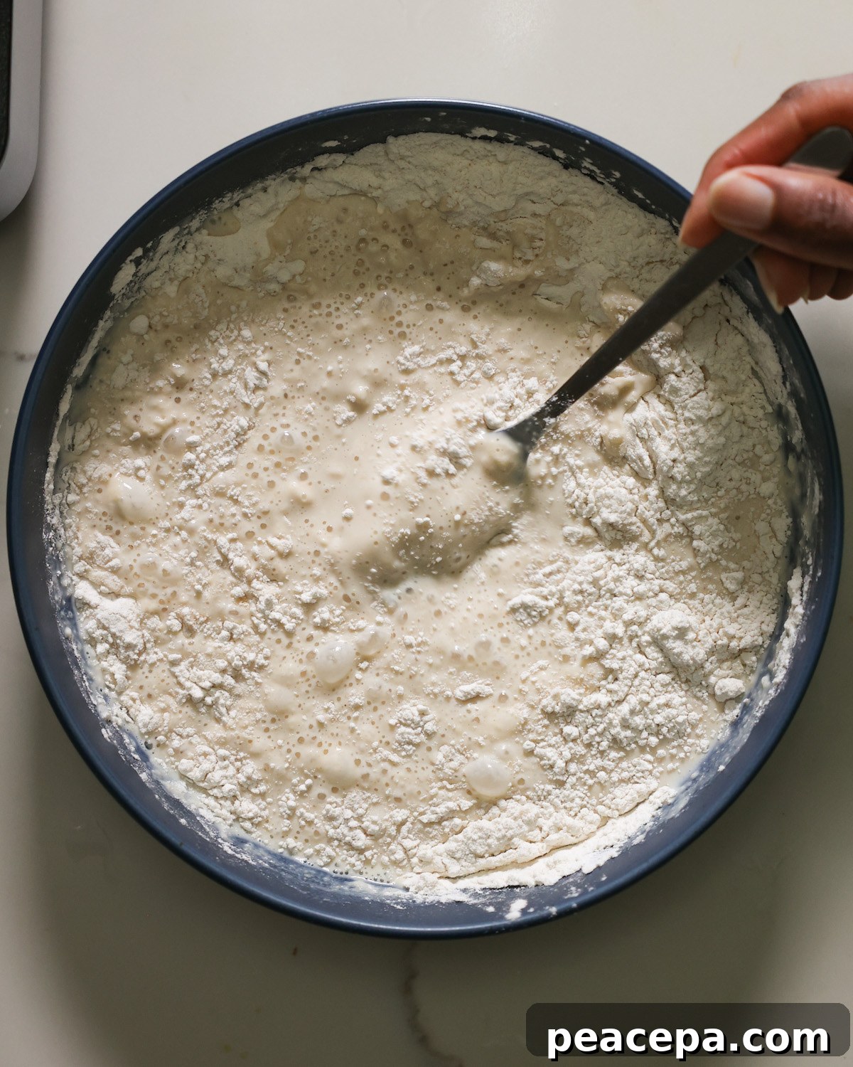 An overhead shot of a brown hand whisking a bowl of the cauliflower batter.