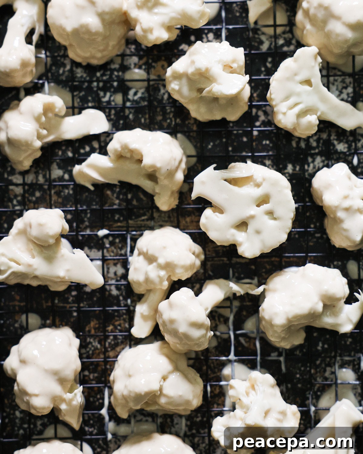 A close-up shot of battered cauliflower on a wire rack-lined baking sheet.