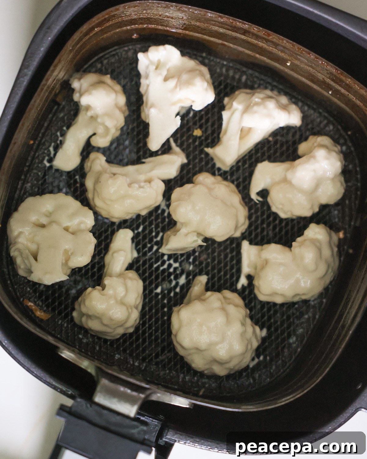 An overhead shot of pieces of battered cauliflower in an air fryer basket.