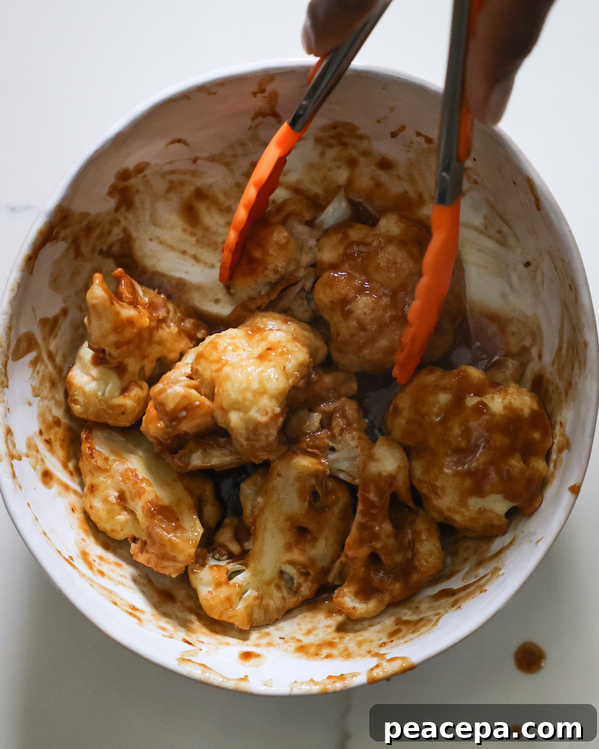 Tossing the cauliflower in the orange sauce in a small mixing bowl.