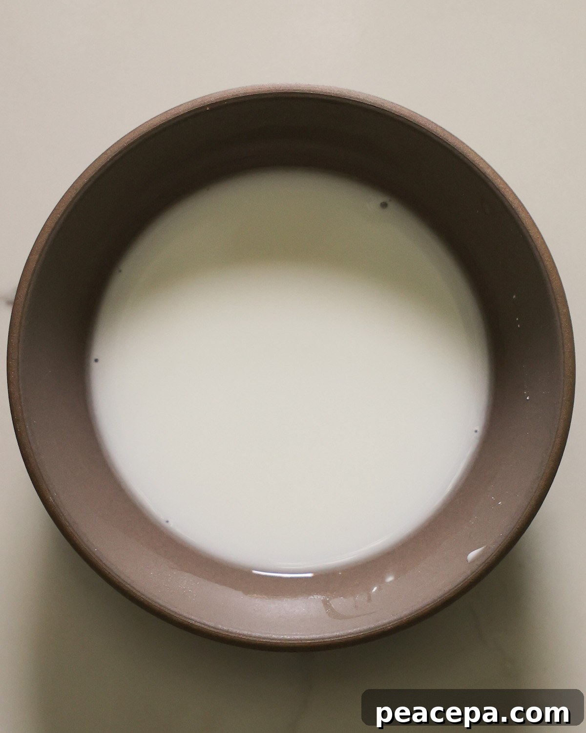 An overhead shot of cornstarch slurry in a small tan bowl.