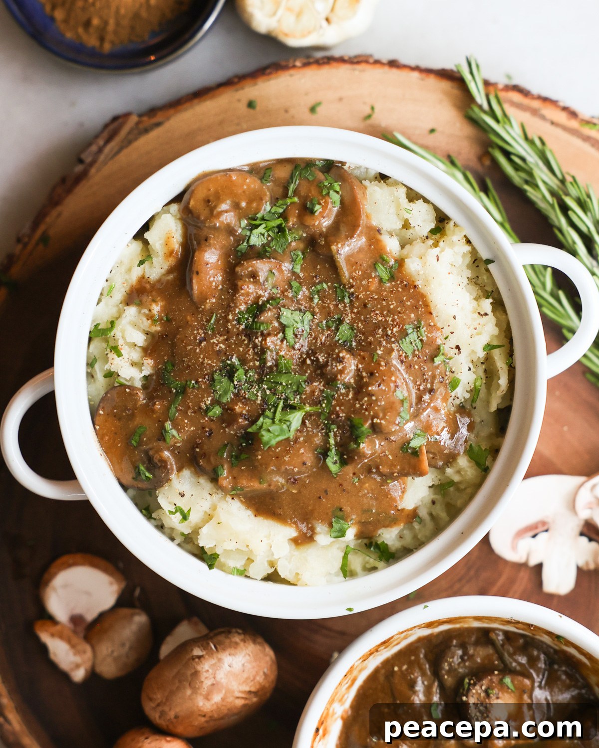 Vegan mashed potatoes and gravy topped with fresh herbs in a bowl on a wooden board.