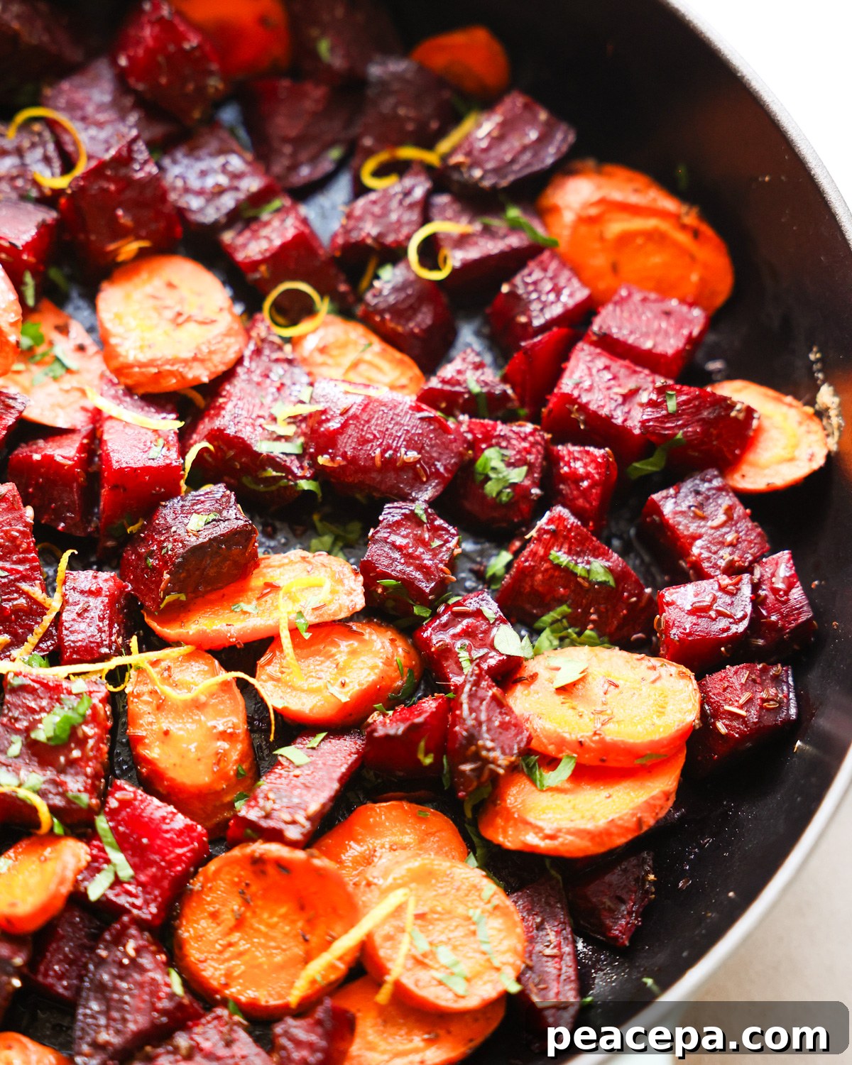 A close-up shot of a bowl of roasted beets and carrots with herbs.
