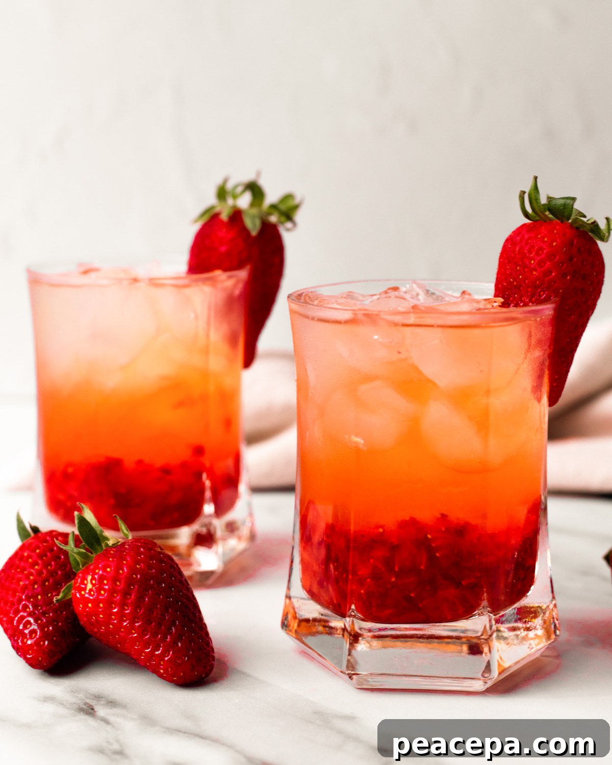 A side shot of two glasses of strawberry rose cocktail with strawberries on the side of the classes.