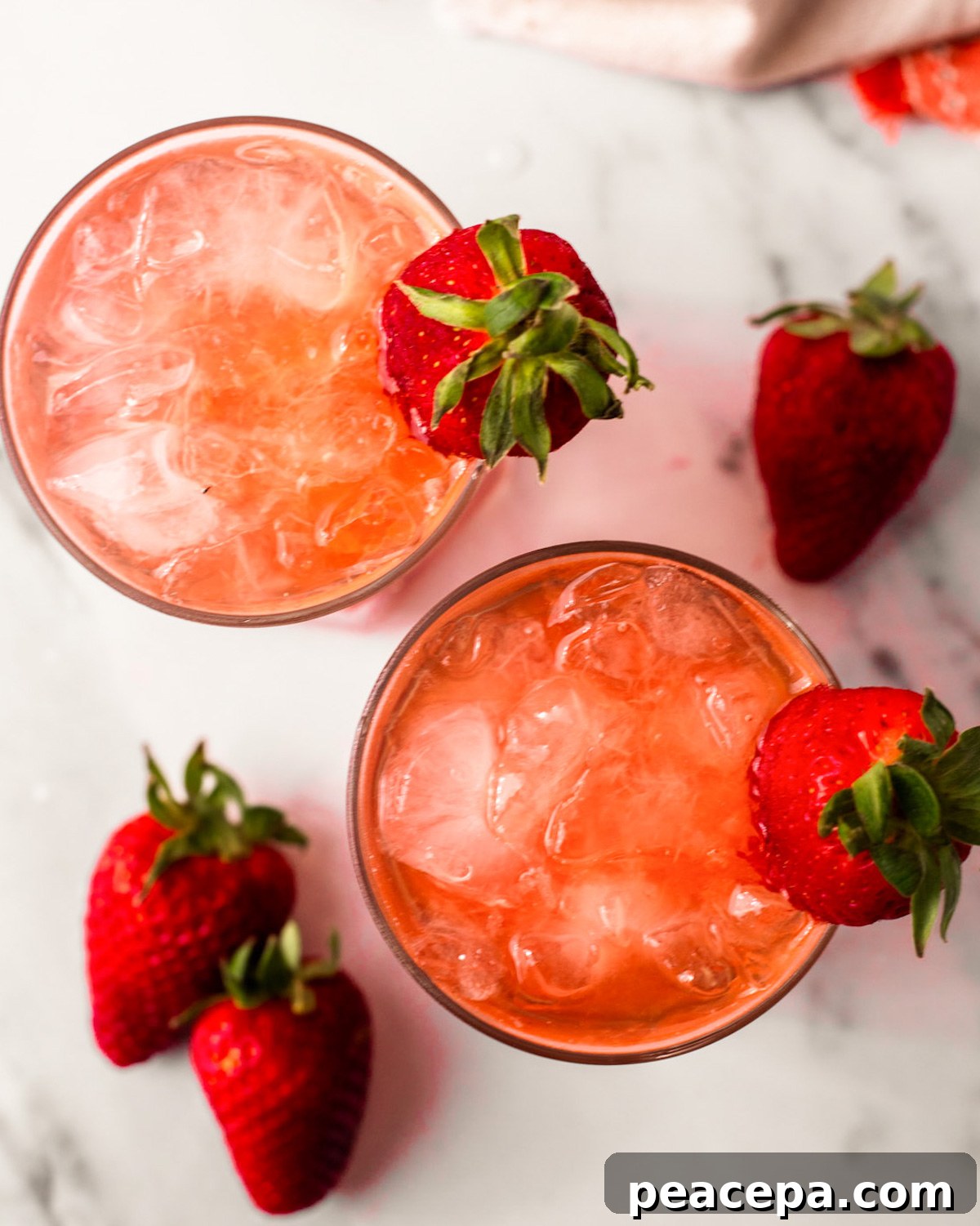 An overhead shot of two glasses of strawberry rose bramble cocktail with strawberries on the side of the glasses.