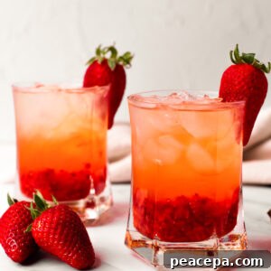 A side shot of two glasses of strawberry rose cocktail with strawberries on the side of the classes.