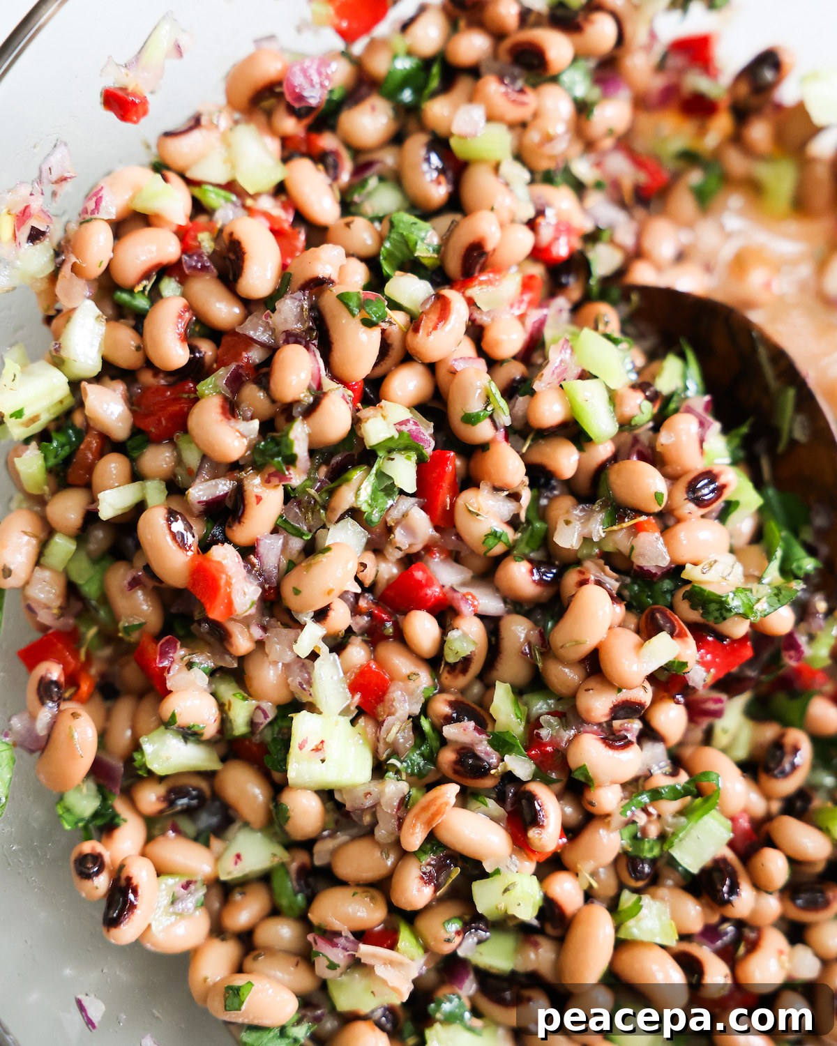 Black eyed pea salad in a glass bowl with wooden spoon