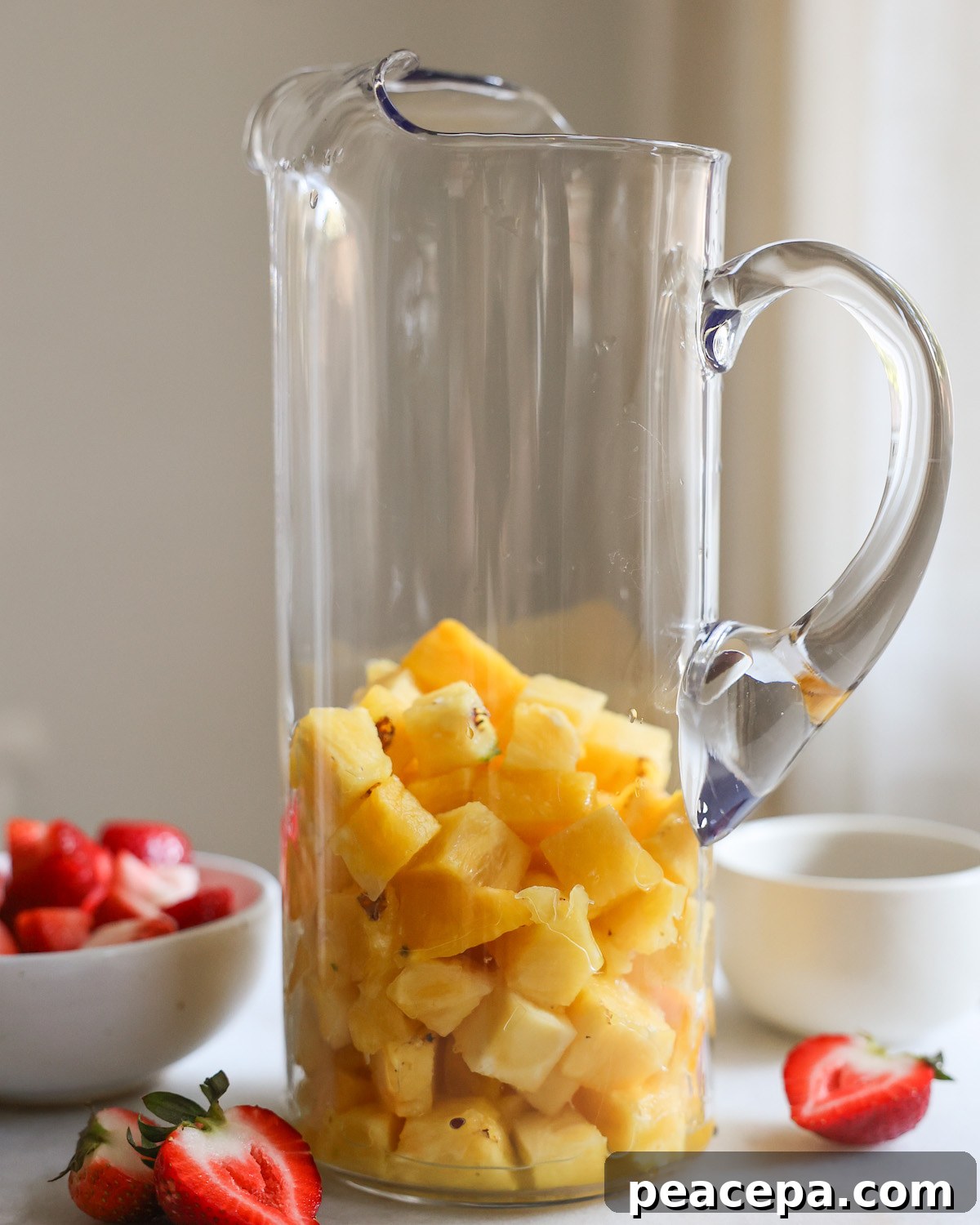 Cubed pineapple in a glass pitcher.