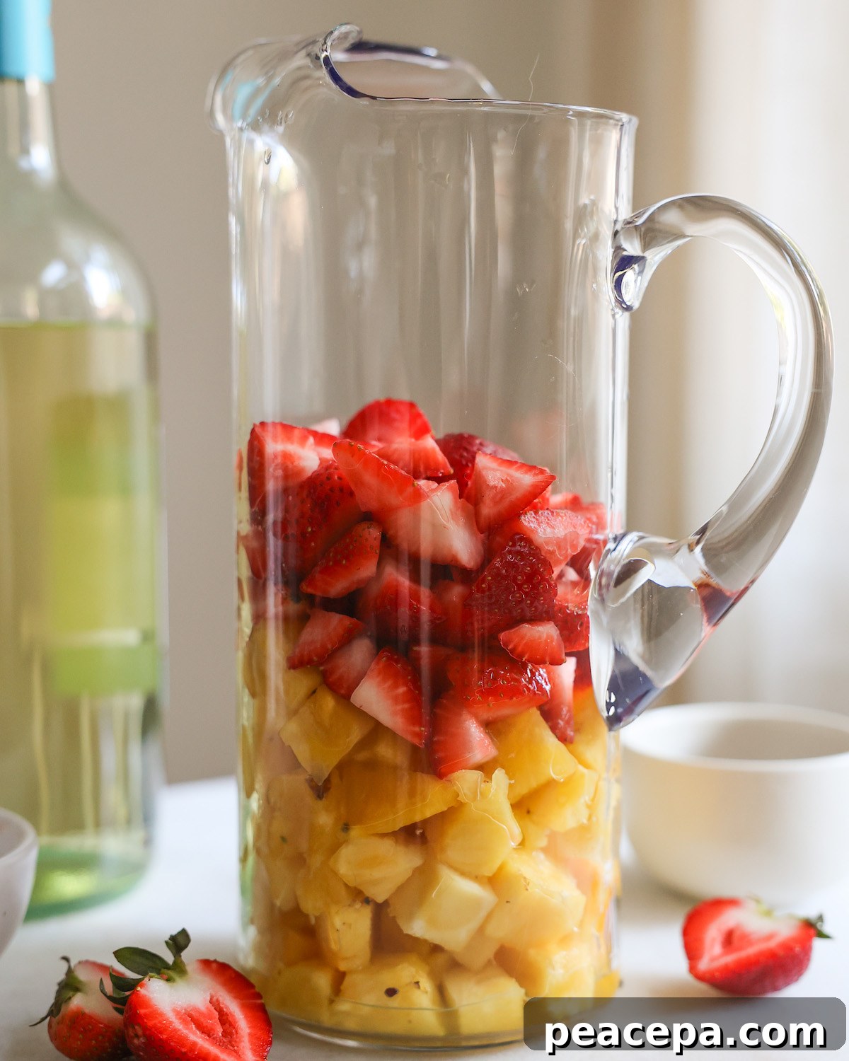 Chopped strawberries and cubed pineapple in a pitcher.