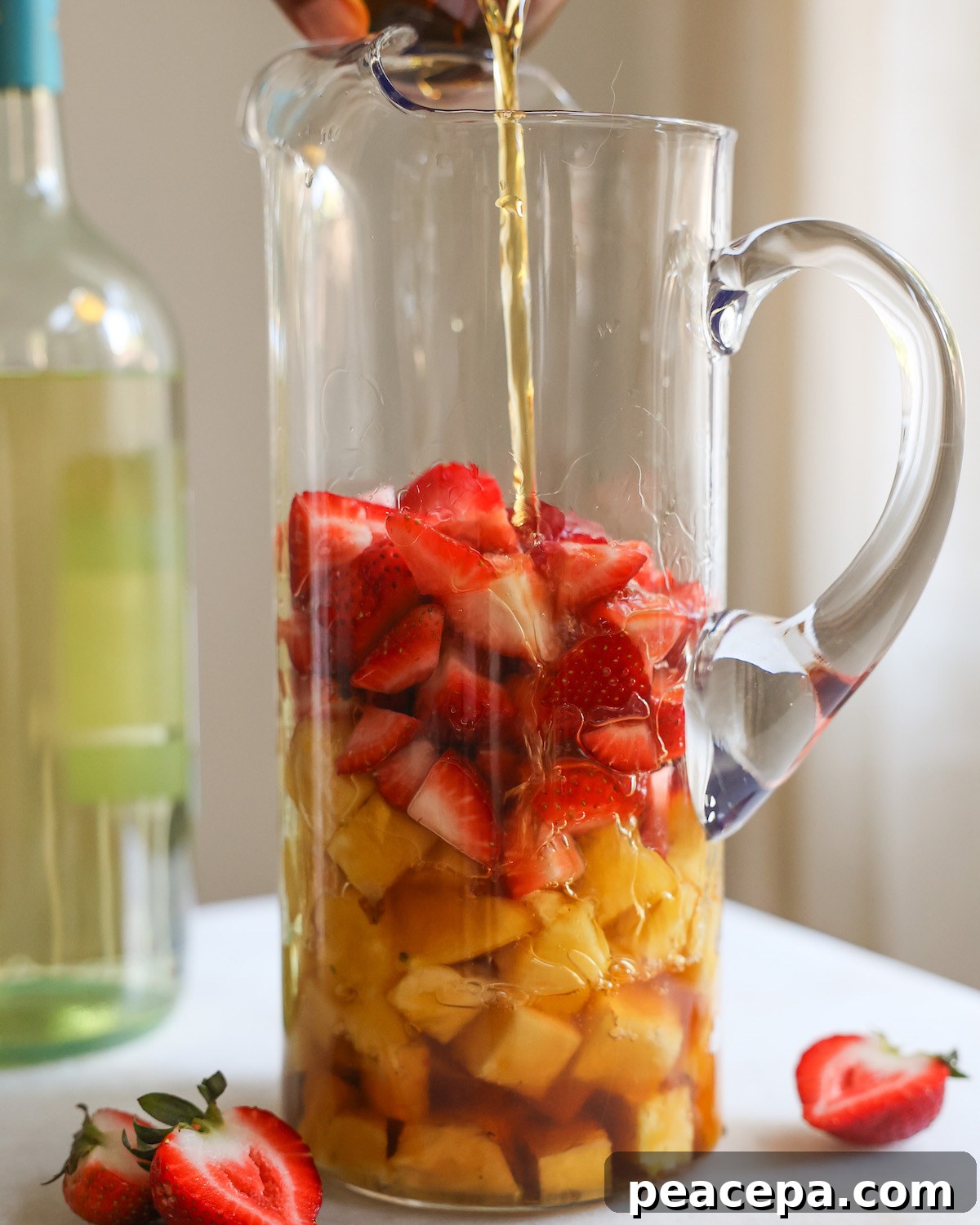 Pouring brandy into a pitcher with strawberries and pineapple.