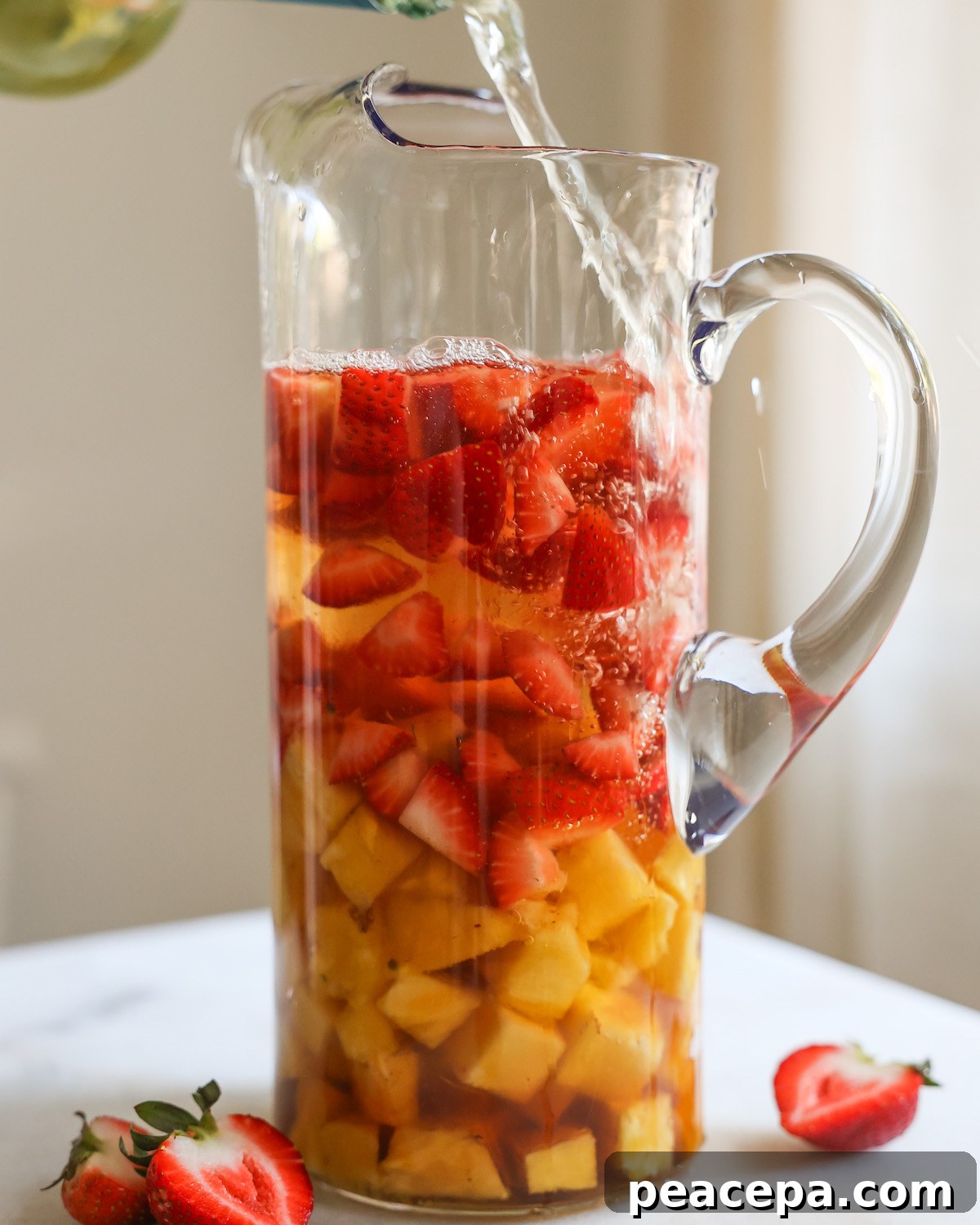 Pouring white wine into a glass pitcher with strawberries and pineapple.