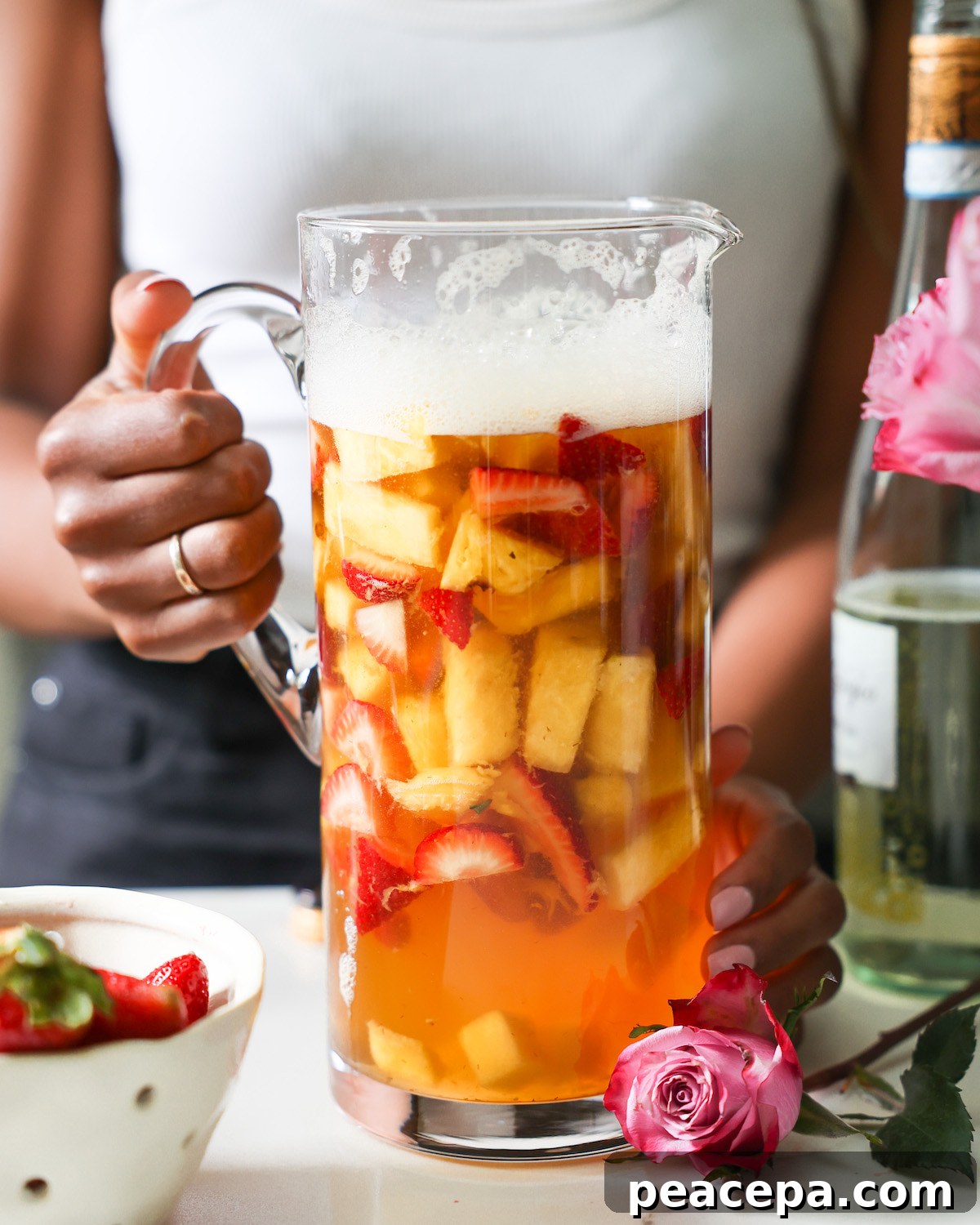 A close-up of Jenné Claiborne holding a pitcher of pineapple summer sangria.
