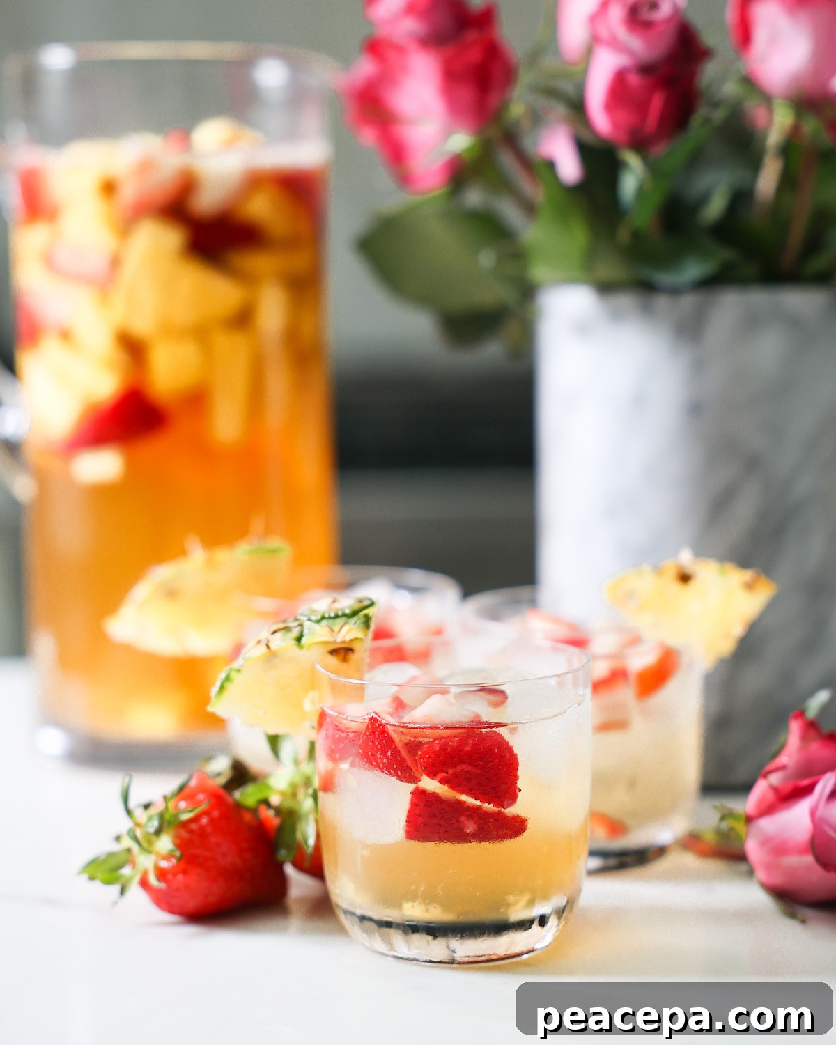 Small glasses of pineapple summer sangria on the counter in front of a pitcher and roses.