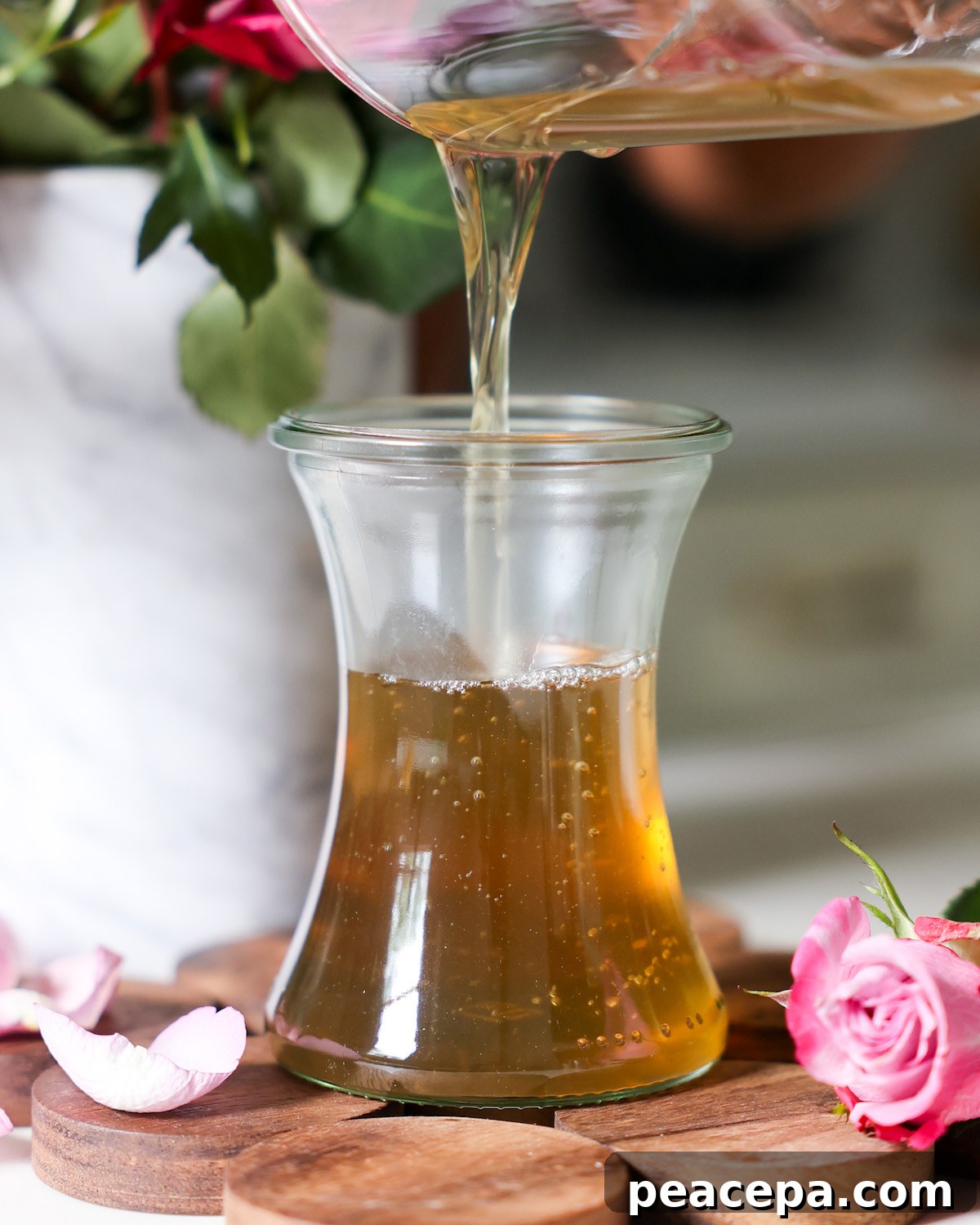 Rose simple syrup being poured into a glass jar.