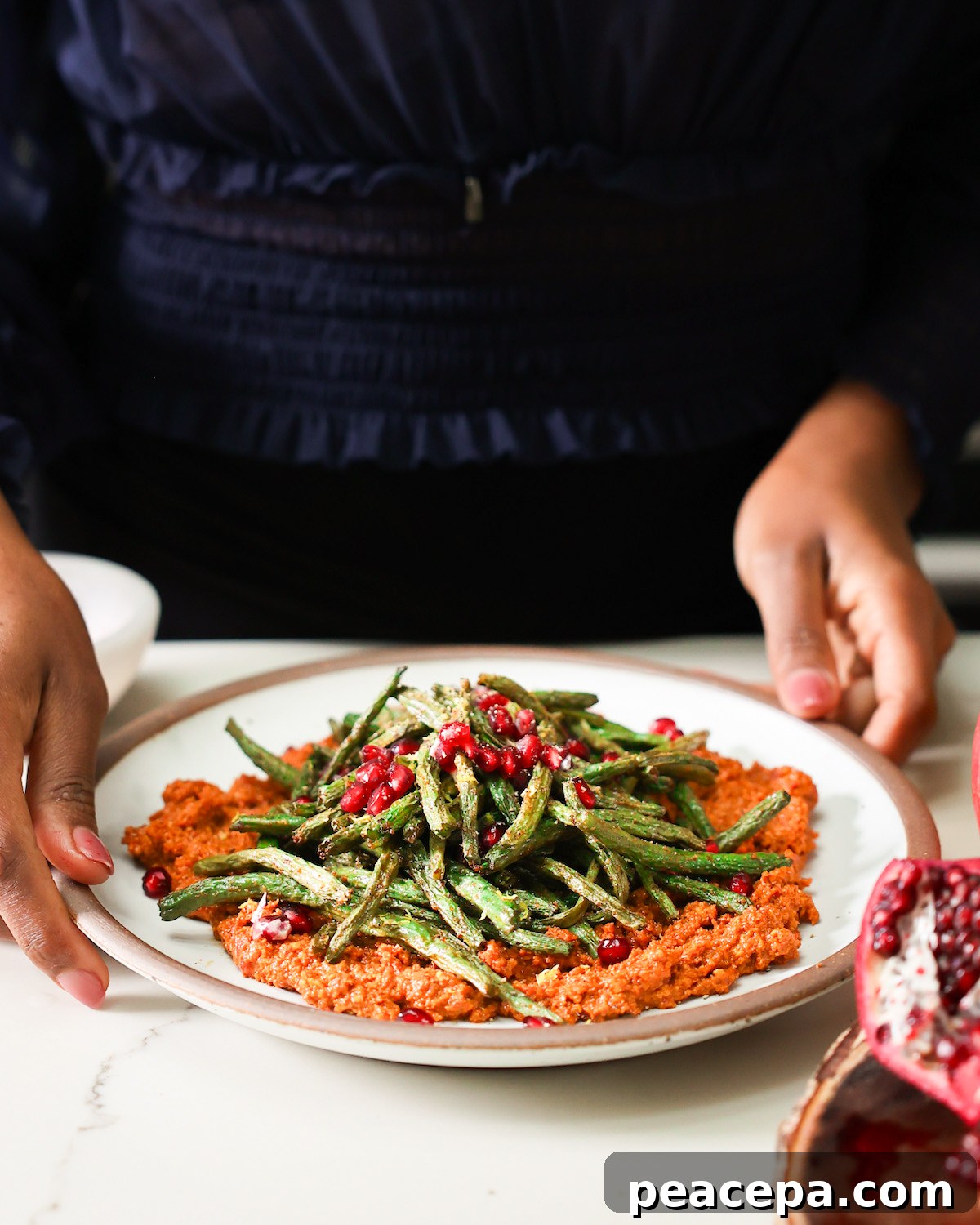 Jenné serving air fryer green beans on a plate of muhammara.