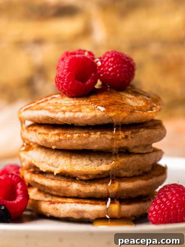 An up-close side shot of a small stack of spelt pancakes with raspberries and maple syrup.
