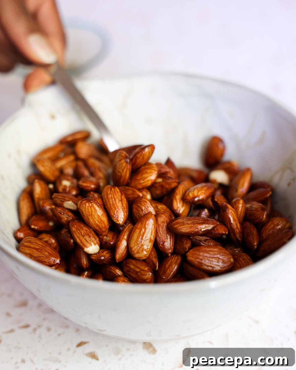 Stirring almonds with tamari in a white bowl before scooping out to drain.