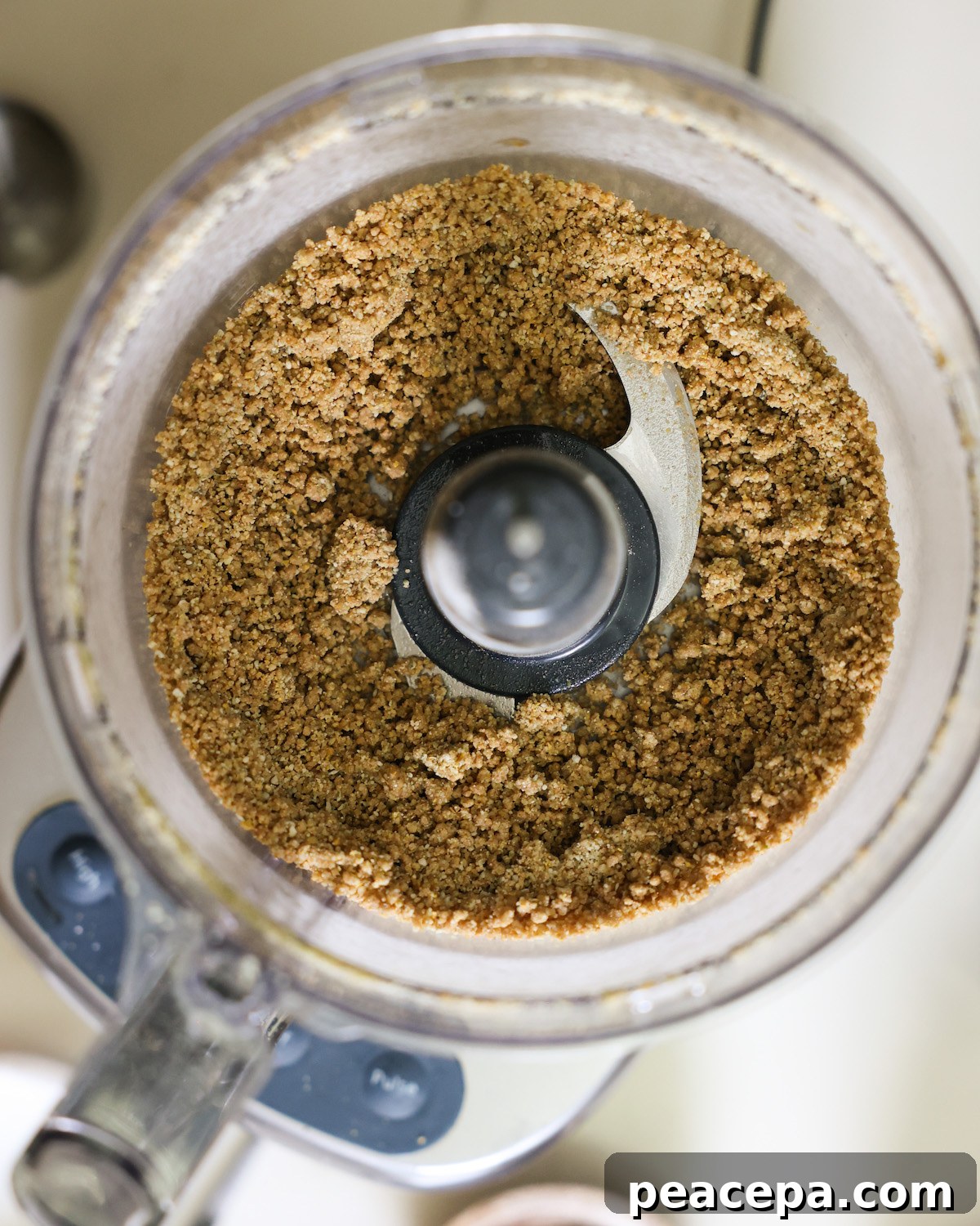 The "cheesy" pumpkin seed cracker meal in the bowl of a food processor before pulsing in the cold water.