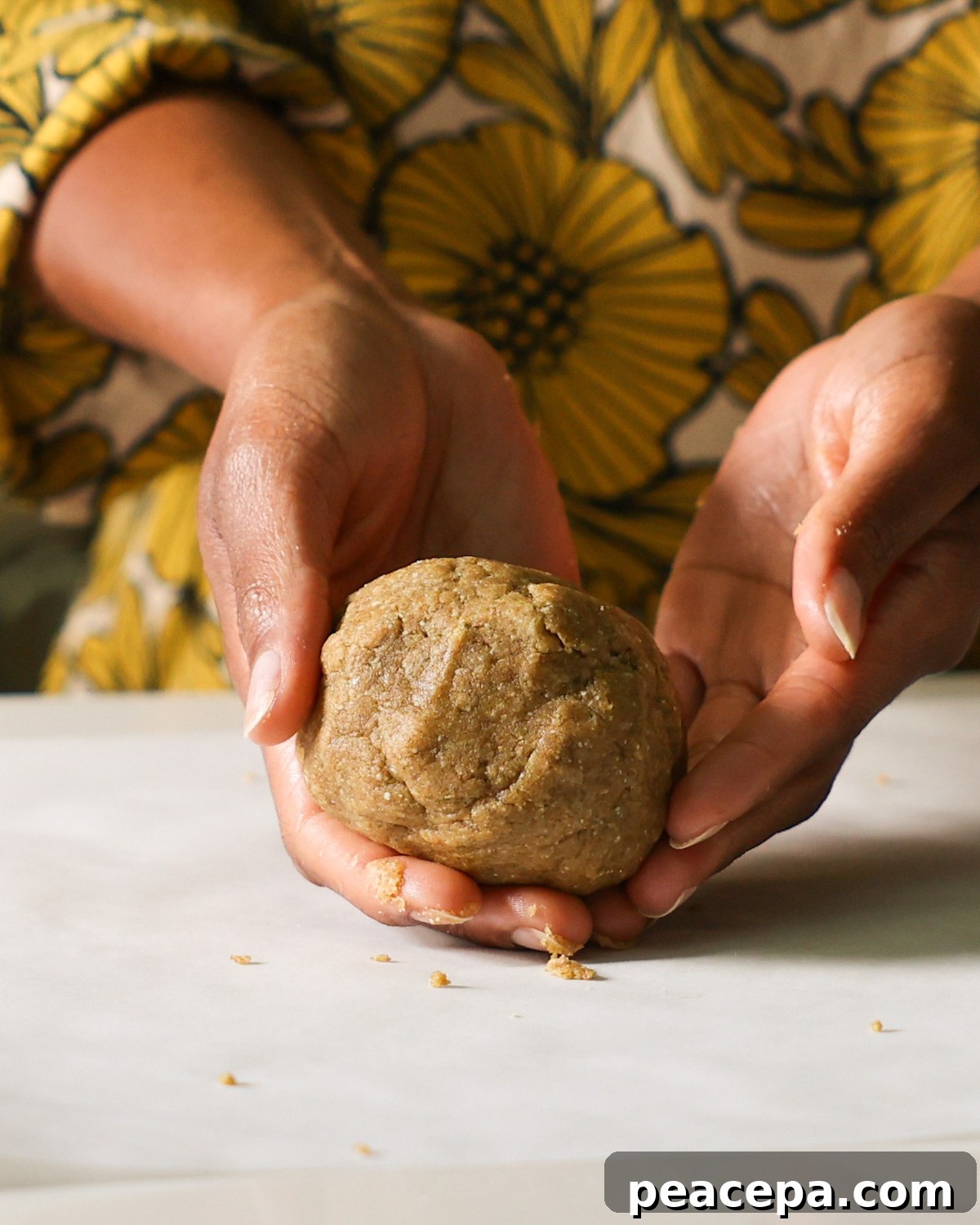 Two hands holding the ball of pumpkin seed cracker dough on the counter.