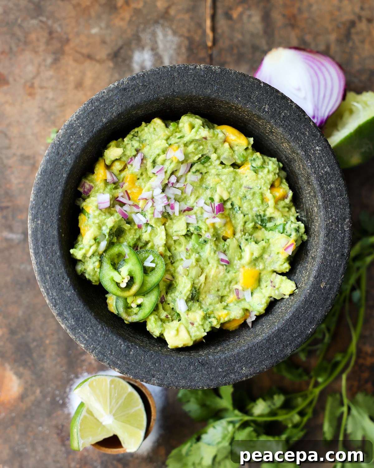 An overhead shot of mango guacamole in a mortar on the counter with red onions and limes.