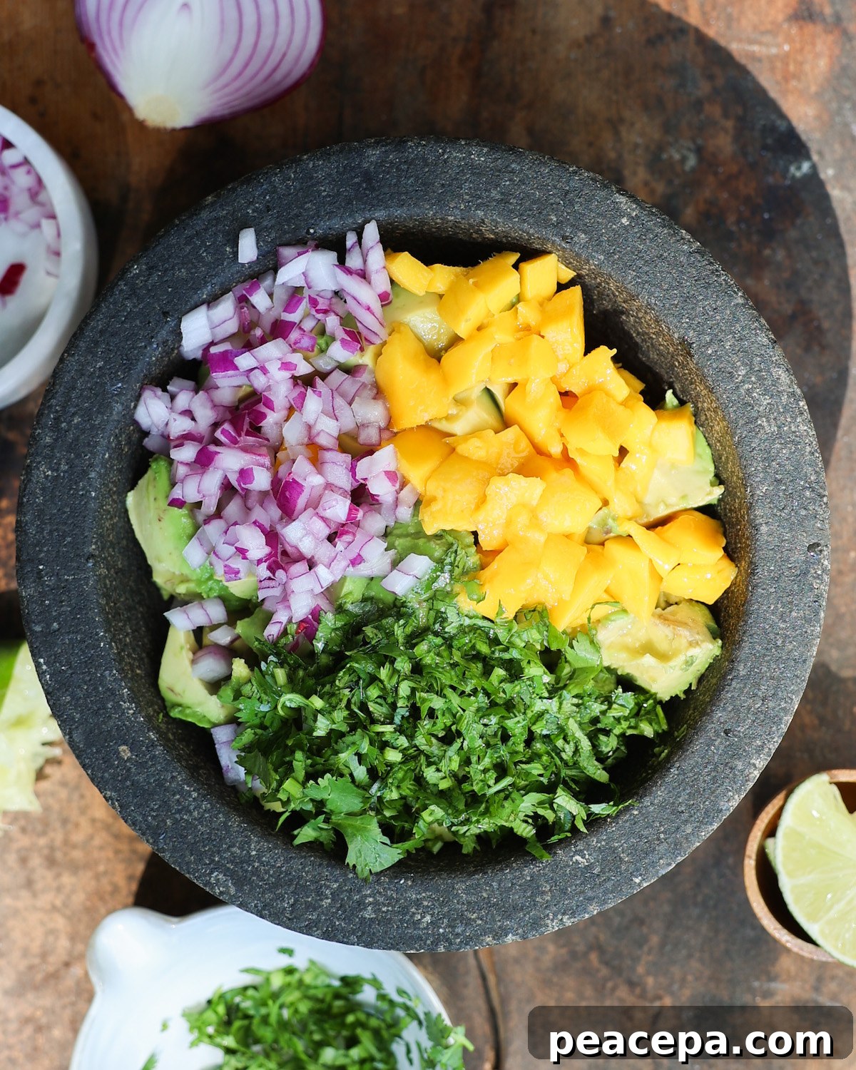 An overhead shot of a mortar with diced onions, cubed mango, cilantro, and avocado.