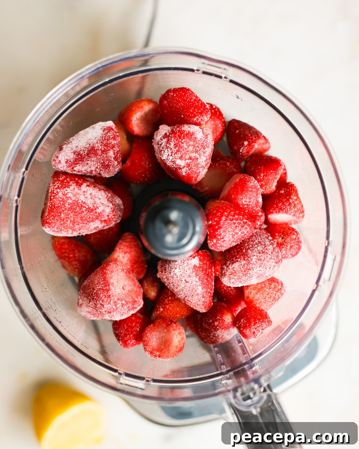 An overhead shot of frozen strawberries in a food processor.