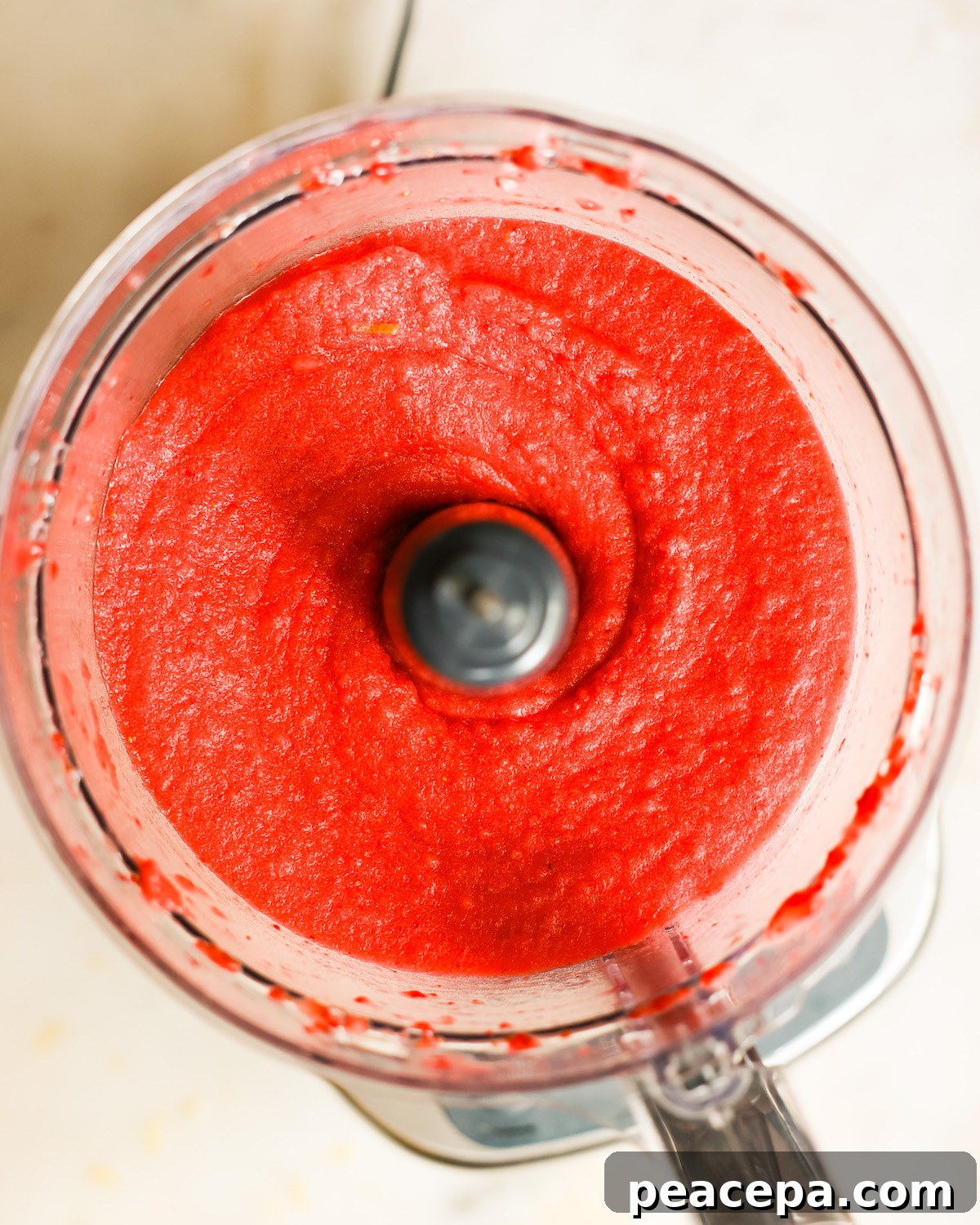 An overhead shot of a food processor full of strawberry sorbet.