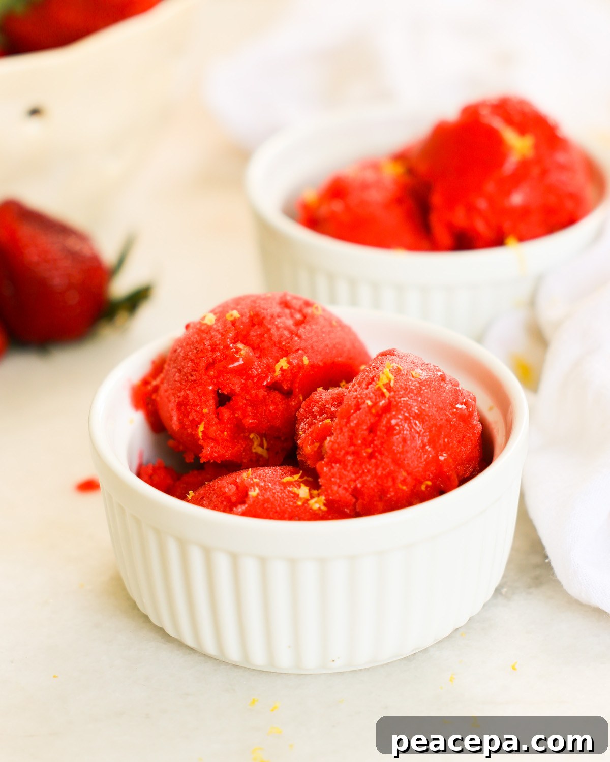 An up-close side shot of two small ramekins of strawberry sorbet garnished with lemon zest.