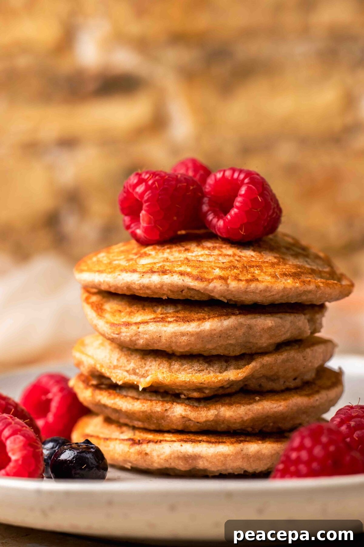 An up-close side shot of a small stack of spelt pancakes with raspberries and no syrup.