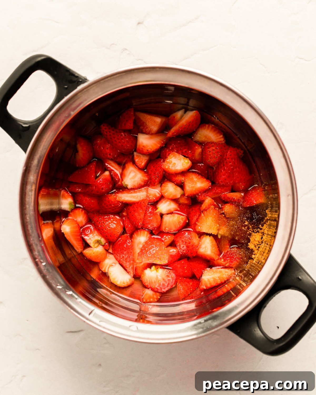 An overhead shot of diced strawberries, water, and cane sugar in a small pot.