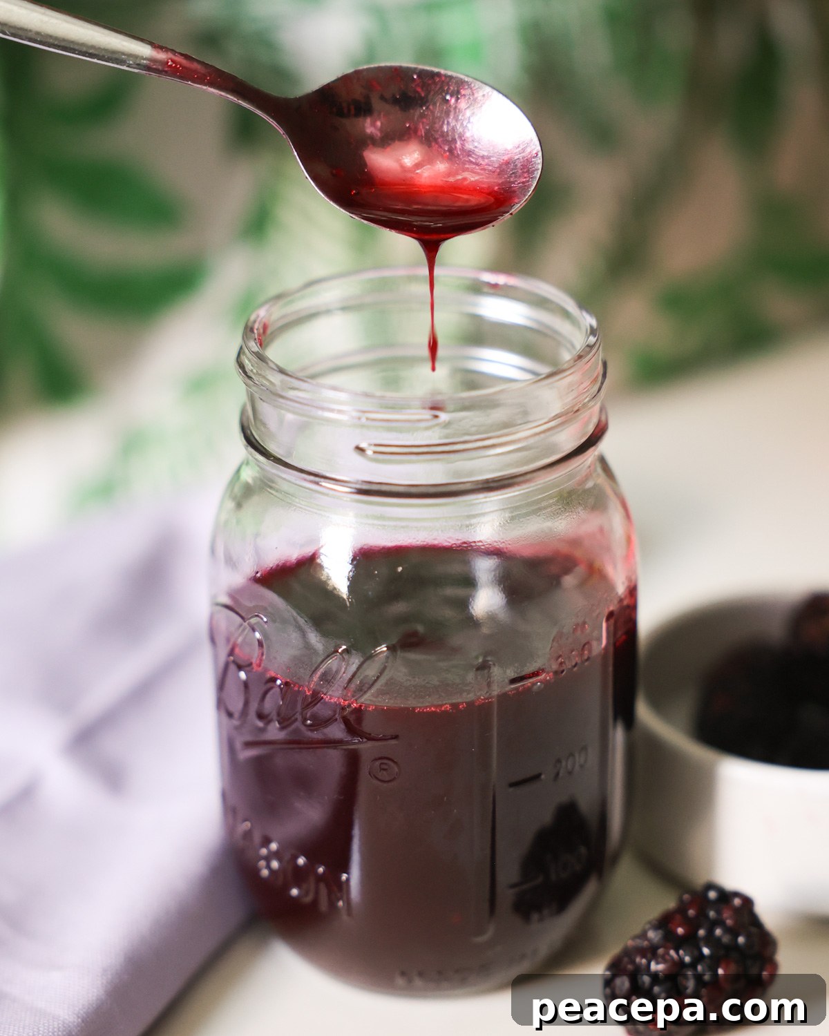 spoon drizzling blackberry syrup over jar