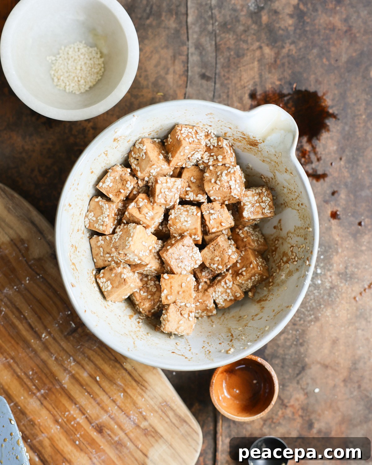 Tofu cubes tossed with sesame and soy sauce in a white mixing bowl.