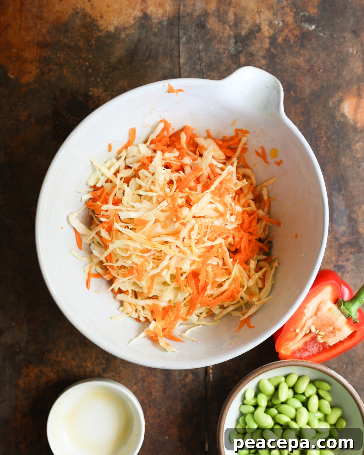 Stirring shredded cabbage and carrots together in a white mixing bowl.