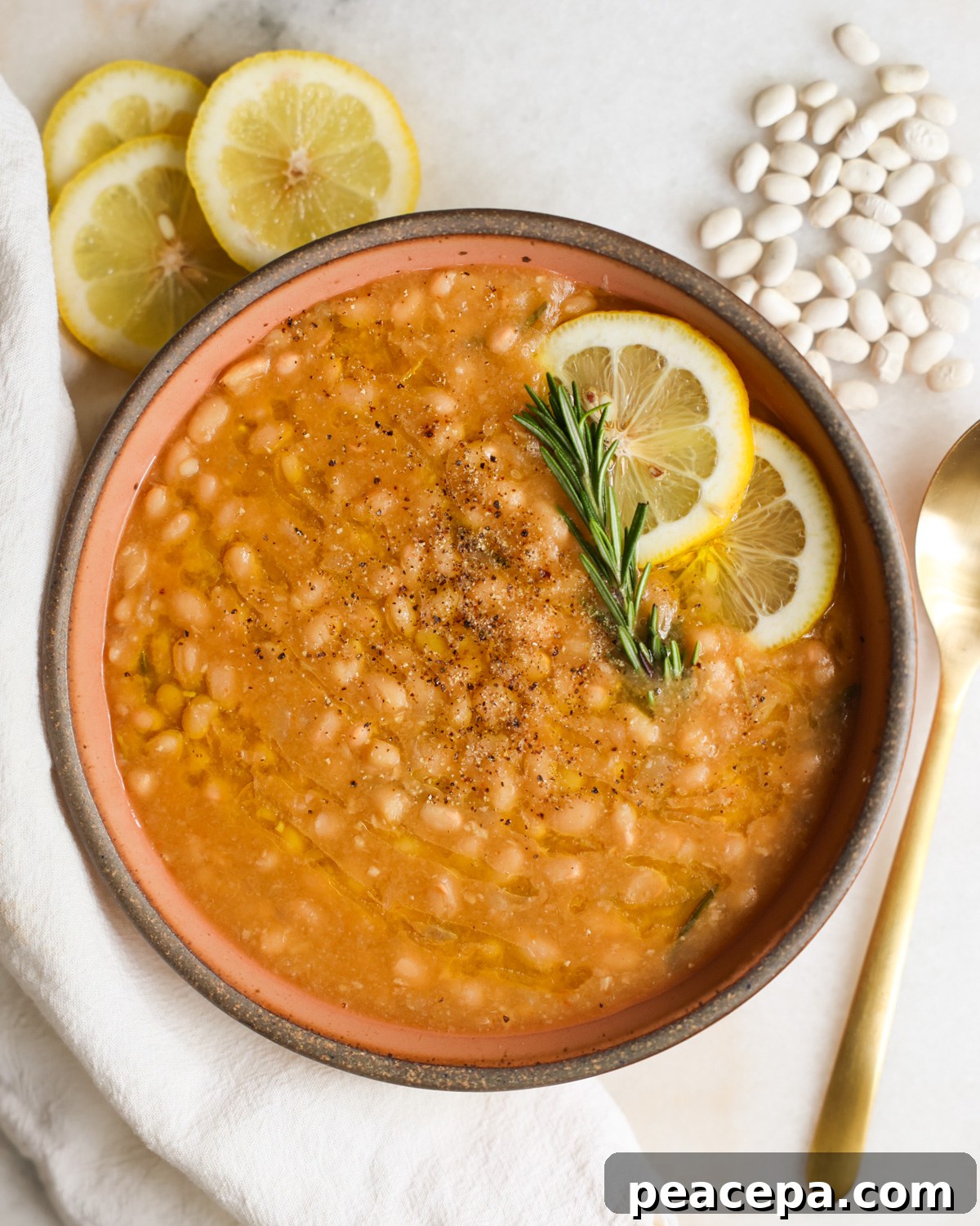 A bowl of Instant Pot white beans with lemon and rosemary garnish.