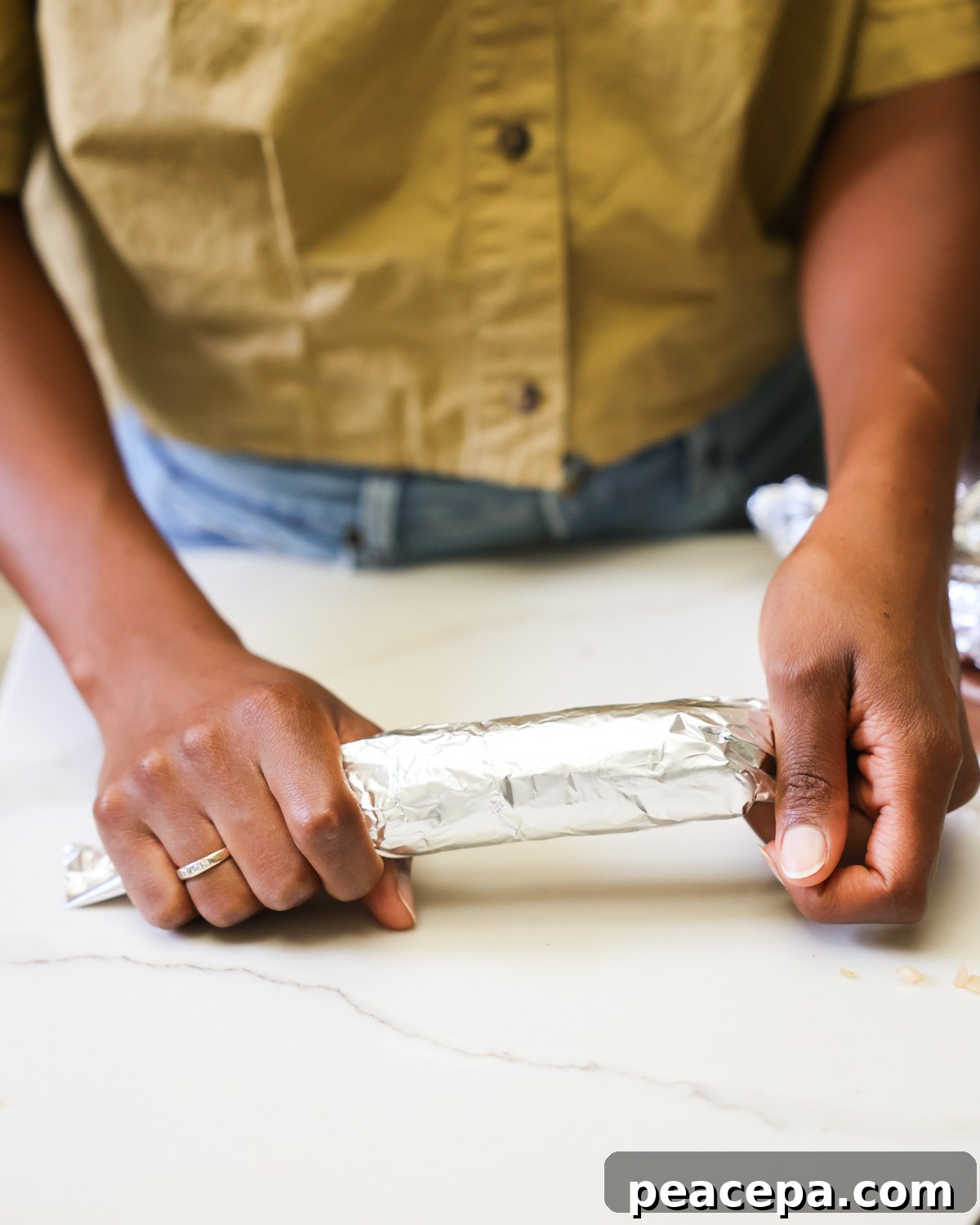 Two brown hands rolling the vegan sausage in the aluminum foil.