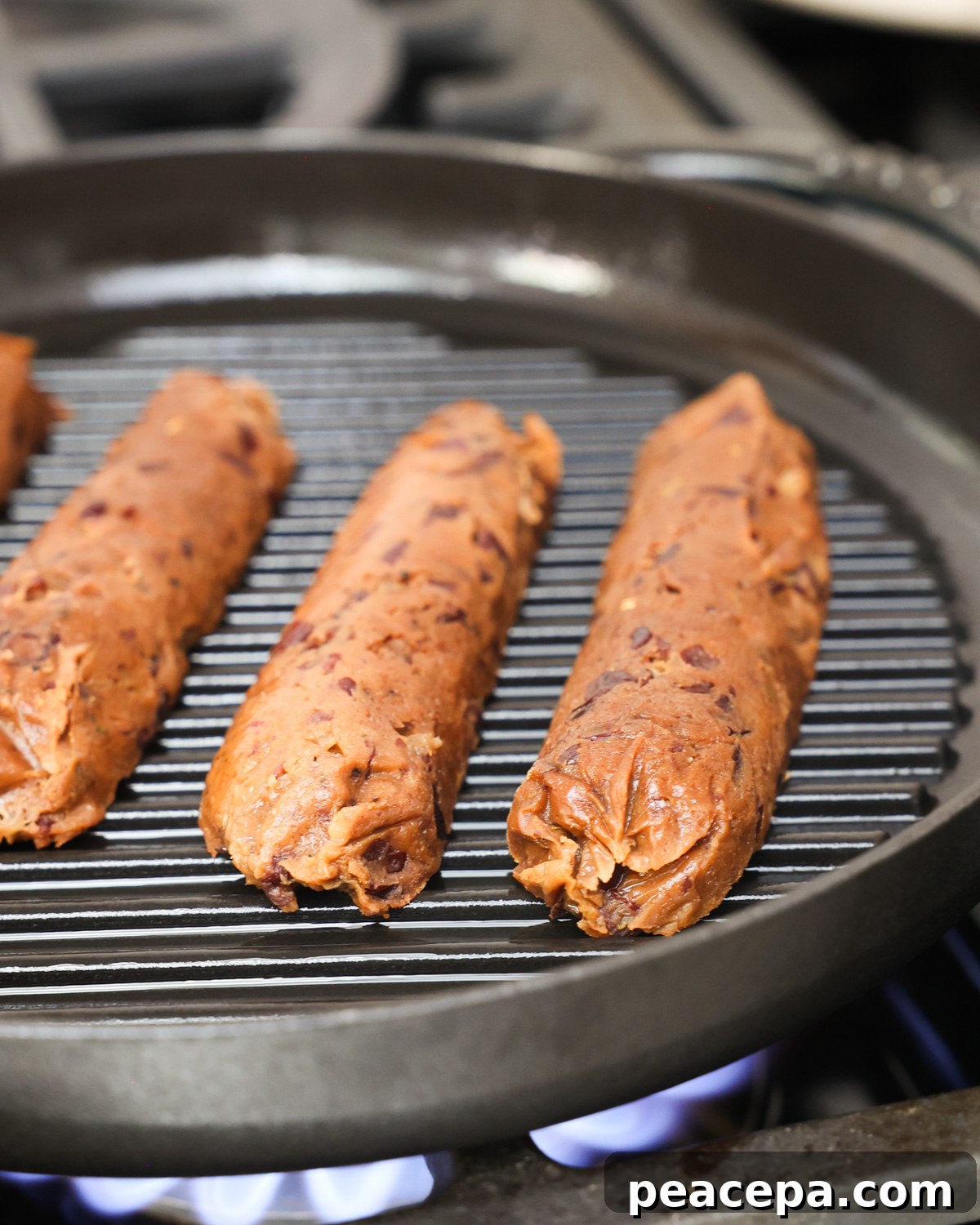A close-up angled side shot of vegan sausages cooking on the stove.