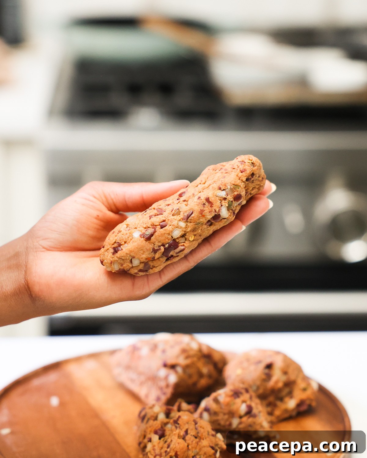 A brown hand holding a shaped vegan sausage.
