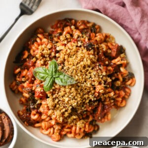 An overhead shot of a white bowl of Instant Pot Vegan Sausage Pasta with bread crumbs and a sprig of basil.