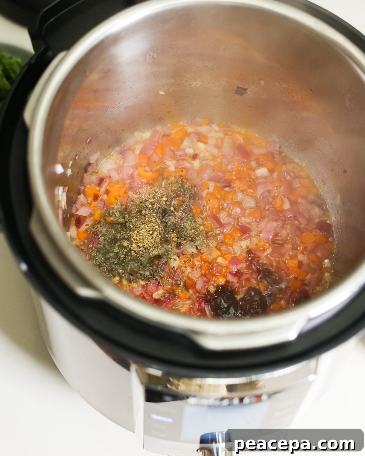 An up-close side shot of aromatics and dried herbs sauteing in an Instant Pot.