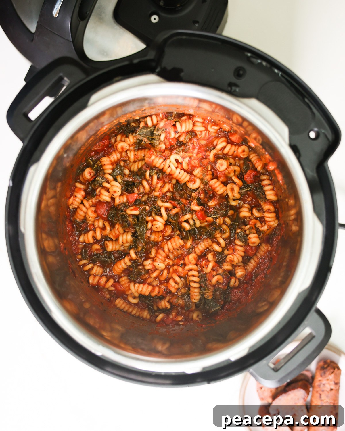 An overhead shot of an Instant Pot full of cooked spiral pasta with red sausage and spinach.