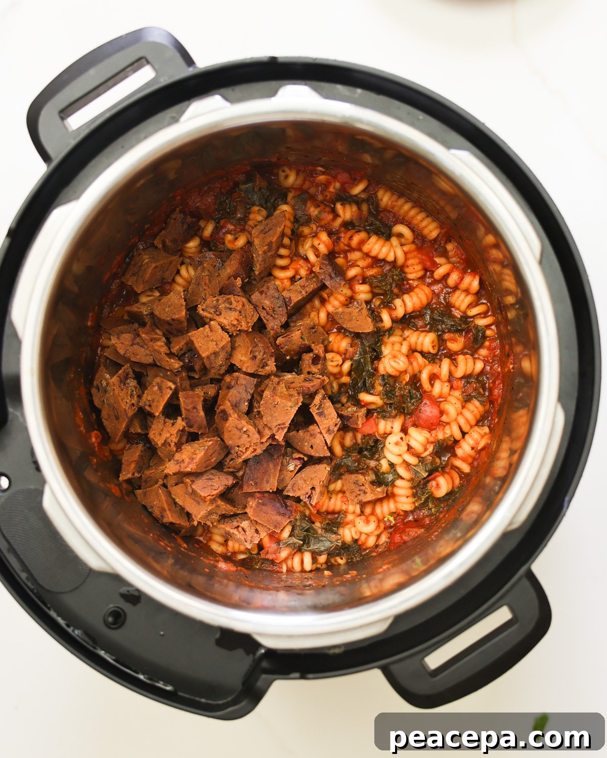 An Instant Pot with cooked pasta and cut up vegan sausage.