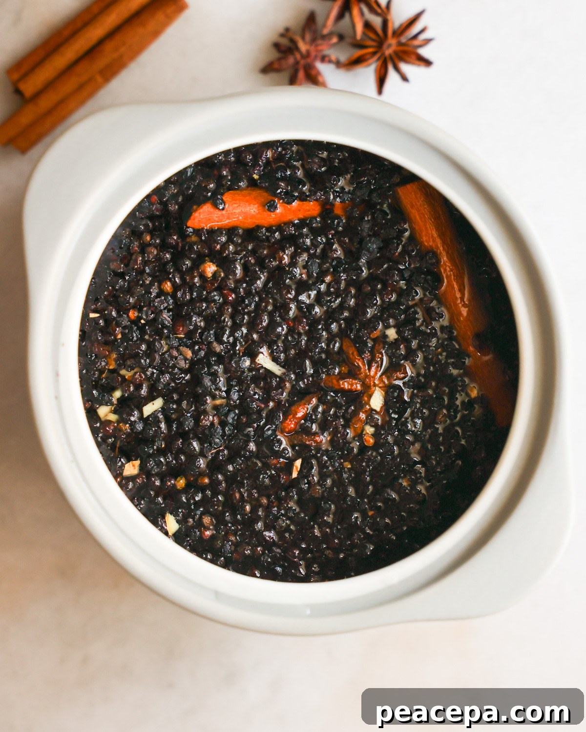 An overhead shot of a crock of elderberries simmered in water with spices.