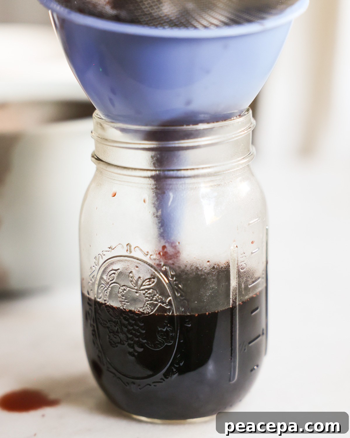 Funneling the elderberry syrup into a glass jar.