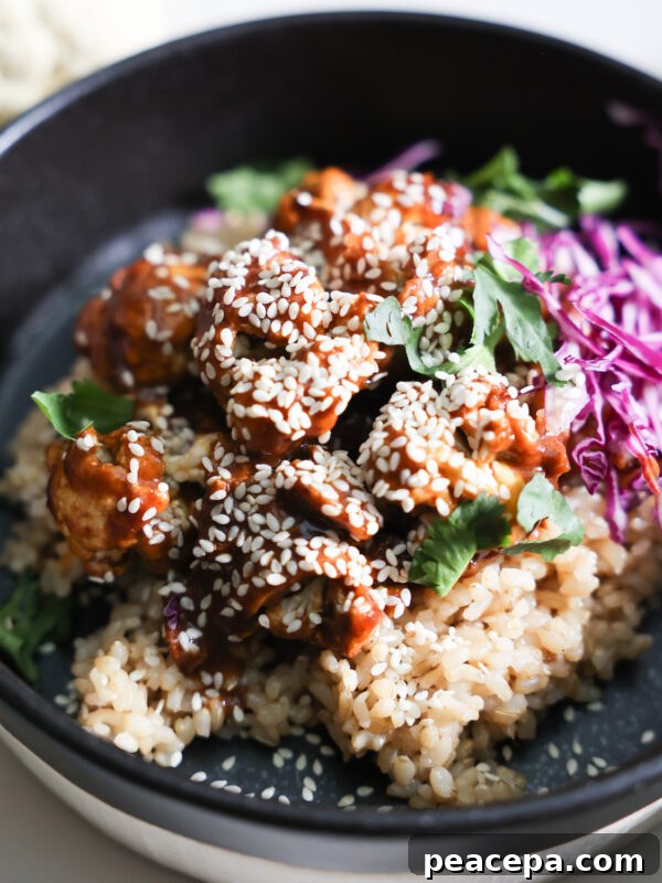 A closeup shot of the orange cauliflower with rice, red cabbage, and cilantro in a black bowl.