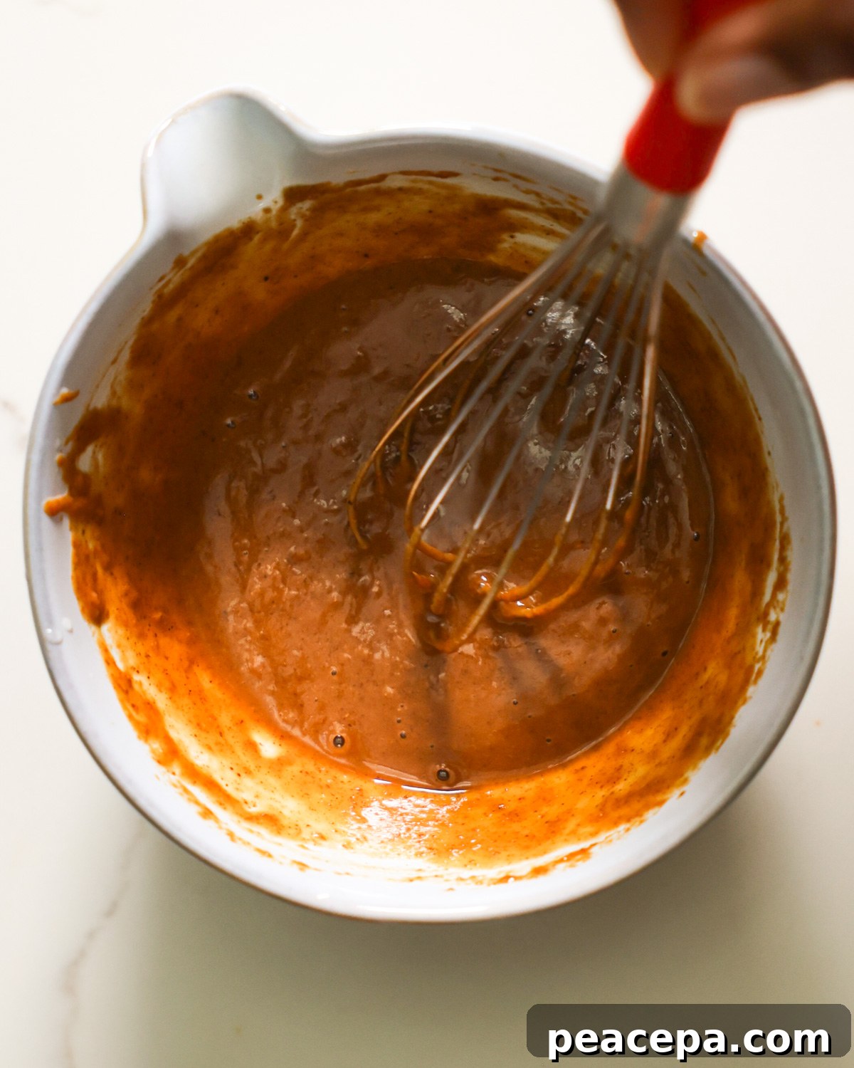 An overhead shot of a brown hand whisking a small bowl of almond lime dressing.