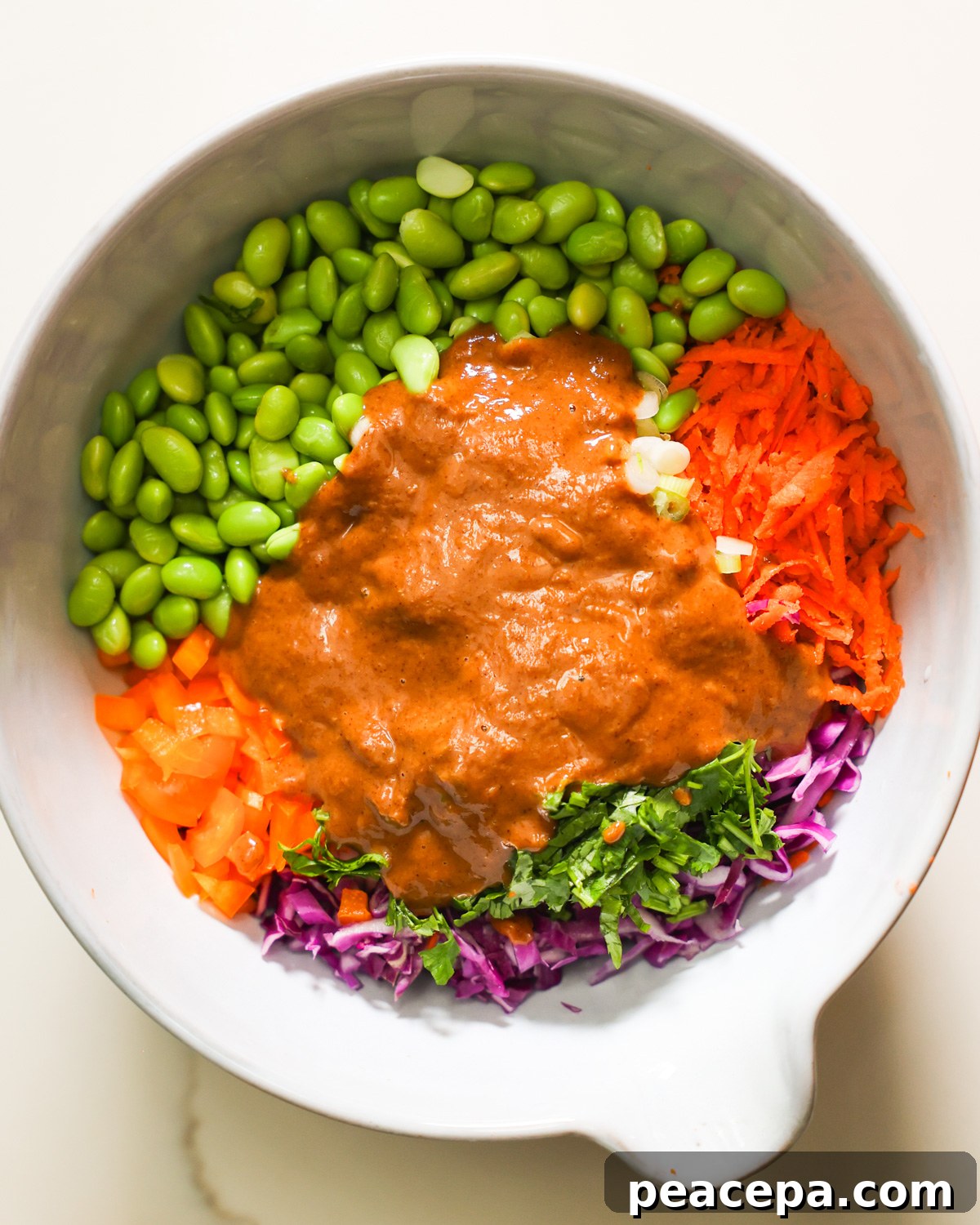 An overhead shot of a mixing bowl with the almond butter dressing poured over the edamame salad.