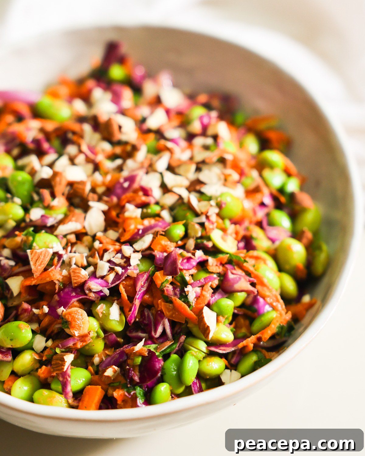 A close-up side shot of a bowl of edamame salad garnished with chopped almonds.