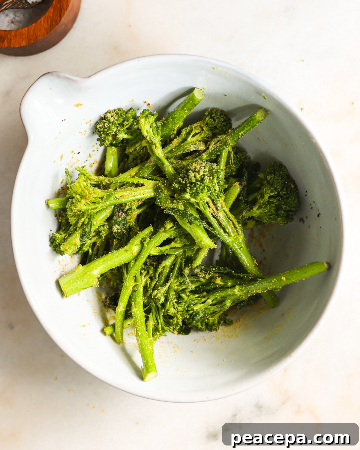 An overhead shot of the seasoned broccolini in a white mixing bowl.