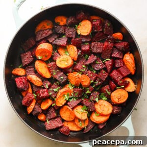 An overhead shot of a white pan of roasted beets and carrots with herbs.