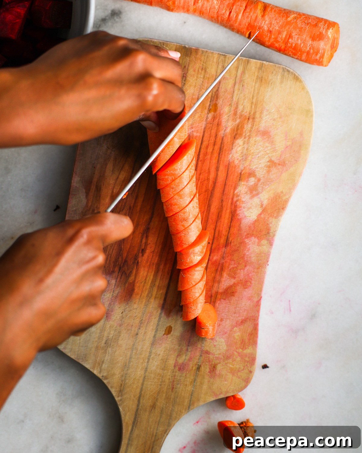 An overhead shot of brown hands slicing carrots on a diagonal.
